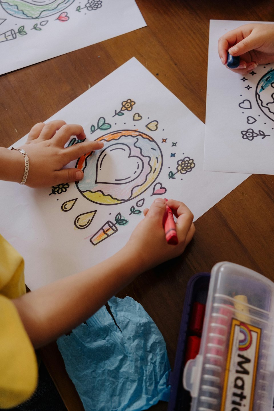 Mani di bambini che colorano disegni con pastelli rossi e blu.